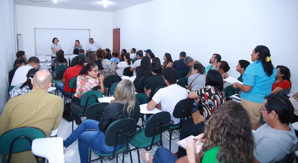 Cerca de 70 pessoas, sentadas, escutam as orientações da equipe que fala à frente, de pé